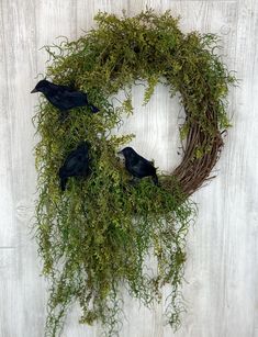 two black birds sitting on top of a green wreath with grass and twigs around it