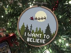 a cross stitch ornament hanging from a christmas tree with the words i want to believe