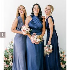 three women in blue dresses standing next to each other and smiling at the camera with flowers behind them