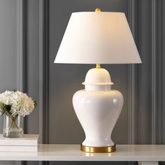 a white table lamp sitting on top of a desk next to a vase with flowers