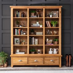 a wooden bookcase filled with lots of books next to potted plants and pots