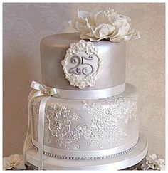 a three tiered wedding cake with white flowers on the top and silver ribbon around it