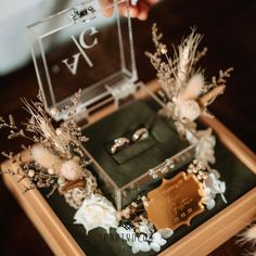 a person holding a ring on top of a box with flowers and feathers in it