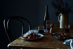 a wooden table topped with plates of food next to a bottle and vase filled with flowers