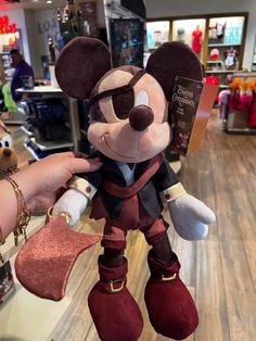 a person holding up a mickey mouse plush toy in a store display case with other items