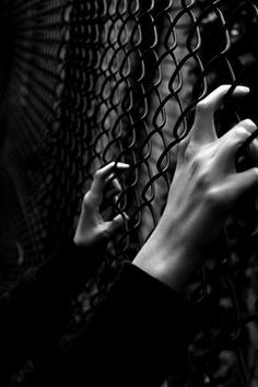 two hands reaching out through a chain link fence