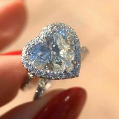 a close up of a person holding a ring with a heart shaped diamond