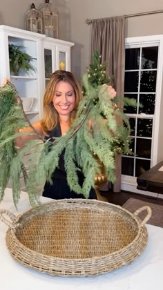 a woman holding up some green plants in front of a basket on top of a table