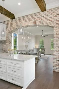 an open kitchen and dining room with brick walls, hardwood flooring and white cabinets