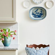 blue and white plates hanging on the wall next to a table with flowers in it