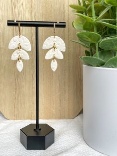 a pair of white flower shaped earrings sitting on top of a table next to a potted plant