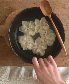 a person holding a wooden spoon over a black bowl filled with dumplings on top of a table