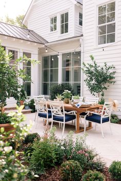 an outdoor dining table and chairs in front of a white house with lots of windows