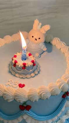 a birthday cake with white frosting and a lit candle in the shape of a bunny