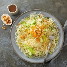 a white plate topped with noodles and veggies next to a cup of sauce