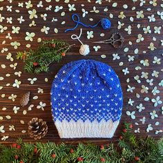 a knitted blue and white hat sitting on top of a wooden table next to pine cones