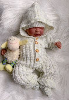 a baby is wearing a white knit outfit and holding a stuffed animal in it's lap