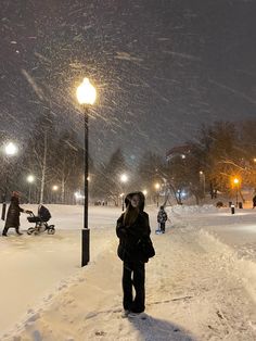 a woman standing in the snow next to a street light