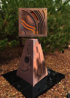 a metal sculpture sitting on top of a pile of leaves next to a pine tree