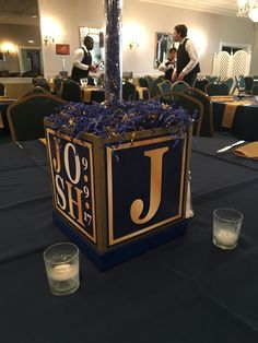 a centerpiece with candles and flowers on a table in a room filled with people