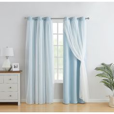 a living room with blue curtains and a white table in front of the window is a potted plant