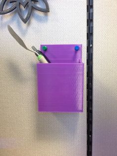 a pair of scissors is stuck in a purple holder on the wall next to a ruler