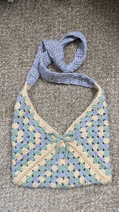 a crocheted purse sitting on the floor with a blue scarf around it's neck