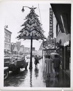 an old black and white photo of people walking down the street in front of a christmas tree