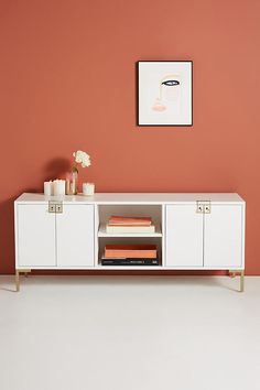 a white cabinet with books and vases on it in front of an orange wall