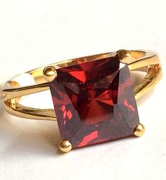 a gold ring with a square shaped red stone in the center and two smaller round stones on each side