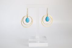 The Gold Double Circle Turquoise Earrings are exquisite jewelry pieces showcasing a pair of interconnected circular charms crafted from gleaming gold. Accented with vibrant turquoise stones, these earrings effortlessly combine a sense of timeless beauty with a pop of color. Turquoise Gemstone Hoop Earrings, Elegant Turquoise Brass Jewelry, Elegant Blue Circular Jewelry, Turquoise Circle Jewelry For Gift, Turquoise Round Gold-plated Jewelry, Turquoise Gold-plated Round Jewelry, Nickel-free Turquoise Circle Jewelry, Elegant Turquoise Hoop Earrings, Turquoise Gold Plated Jewelry With Matching Earrings