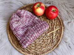 two apples sitting on top of a wicker basket next to an apple in a knitted hat