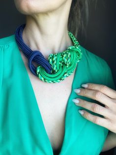 a woman wearing a blue and green necklace with an intertwined knot on it's neck