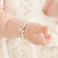 Baby girl wearing the white luster pearl bracelet around her wrist, part of our baby jewelry collection. Baby Pearl Bracelet, Classic White Heart Bracelet For Gifts, Elegant Heart Beads Charm Bracelet For Wedding, Elegant Heart Beads Bracelet As A Gift, Elegant Heart Beads Bracelet Gift, Dainty White Heart Bracelet For Anniversary, Elegant White Heart Bracelet, Elegant White Heart-shaped Bracelet, Classic Heart Charm Bracelet For Wedding