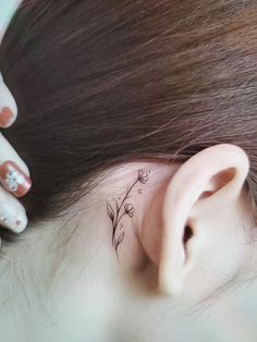 a woman's ear has a small flower tattoo on it