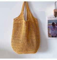 a yellow crocheted bag hanging on the wall next to a magazine and photo