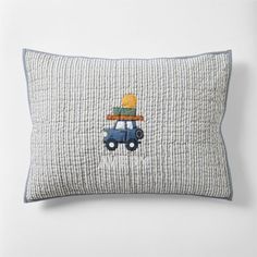 a blue and white pillow with a small toy car on it's back, embroidered onto the front