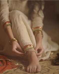 a woman in white dress sitting on the ground with her legs crossed and wearing gold bracelets