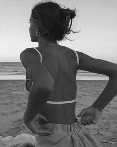 a woman standing on top of a sandy beach next to the ocean with her back turned