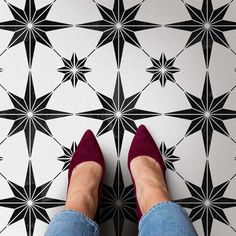 a woman's feet in red shoes standing on a black and white tile floor