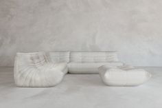 a white couch sitting on top of a cement floor next to a chair and ottoman