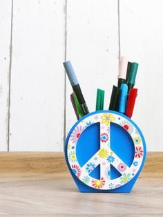 a peace sign pen holder with pens and pencils in it on a wooden table