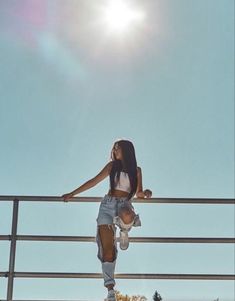 a woman standing on top of a metal rail next to a sun filled blue sky