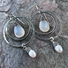 Two tiny genuine freshwater pearls are carefully wrapped in sterling silver wire. The white pearls dangle from sterling silver rings which I have formed, soldered, and hammered by hand. Inside the rings are natural Chalcedony teardrops. The earrings dangle from handformed Sterling Silver earwires. The silver has been oxidized and polished to create the patina finish. Be sure to see all photos and video for size and color reference. Total Earring Length: About 2 inches Wire Wrapped Teardrop Pearl Jewelry, Sterling Silver Teardrop Pearl Drop Jewelry, Sterling Silver Teardrop Dangle Earrings With Pearl Drop, White Teardrop Wire Wrapped Earrings, Silver Teardrop Pearl Earrings With Ear Wire, Sterling Silver Teardrop Pearl Earrings With Charm, Silver Teardrop Wrap Earrings, White Teardrop Wire Wrapped Pearl Earrings, Handmade White Sterling Silver Teardrop Earrings