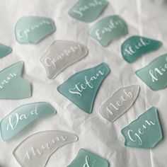 glass name tags with names on them sitting on a white table cloth covered in tissue paper