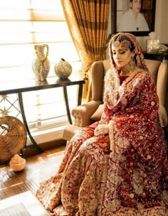 a woman sitting in a chair wearing a red and gold bridal gown with an elaborate headpiece