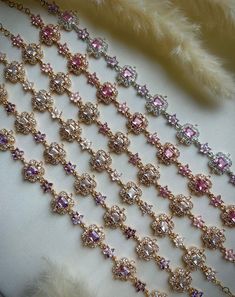 an assortment of fancy necklaces and bracelets are displayed on a white cloth with feathers