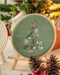 two cross stitch christmas trees sitting next to each other on wooden easels with pine cones