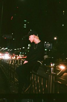 a man sitting on top of a metal fence next to a city street at night