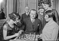 an old black and white photo of some people playing chess with other people in the background